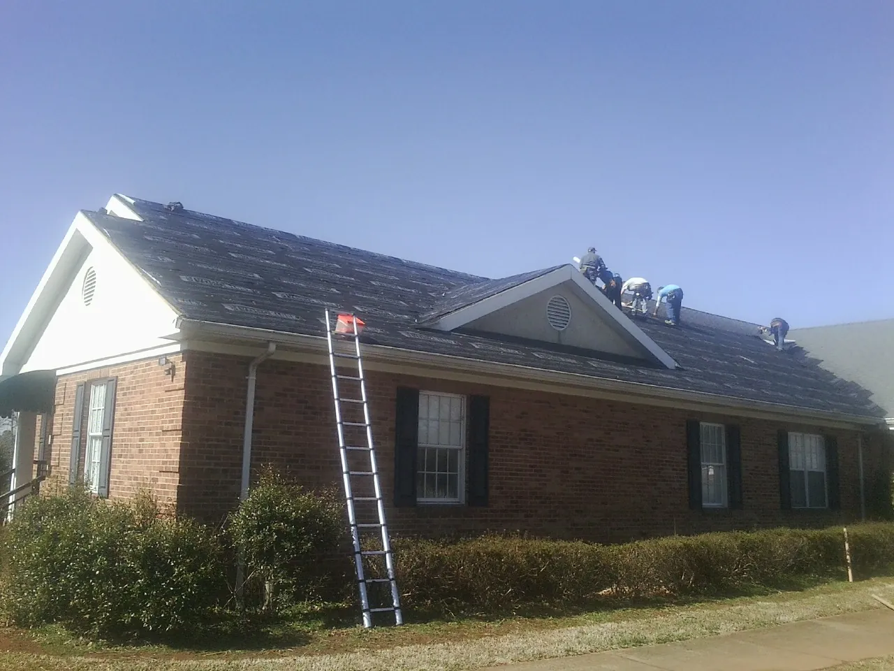 Crew tearing shingles off a brick ranch roof with a ladder set — Metal Roof Repair work by our crew in Waukomis