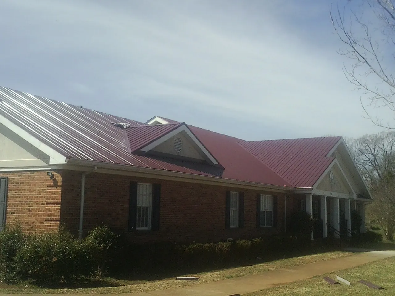 Red metal roof with gabled entries on a long brick building, from a Hail Damage Roof Repair job in Waukomis
