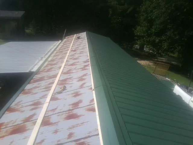 Old rusted panels beside newly installed green metal roofing — Wind Damage Roof Repair by Roofing Brothers in Waukomis