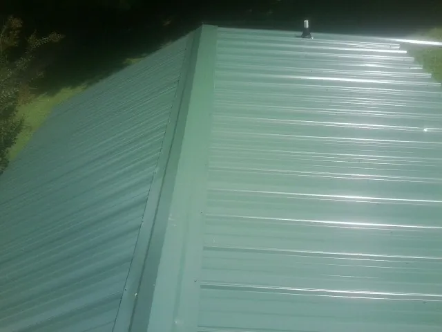 New green metal panels meeting at the ridge of a roof — Flat Roof Repair work by our crew in Waukomis