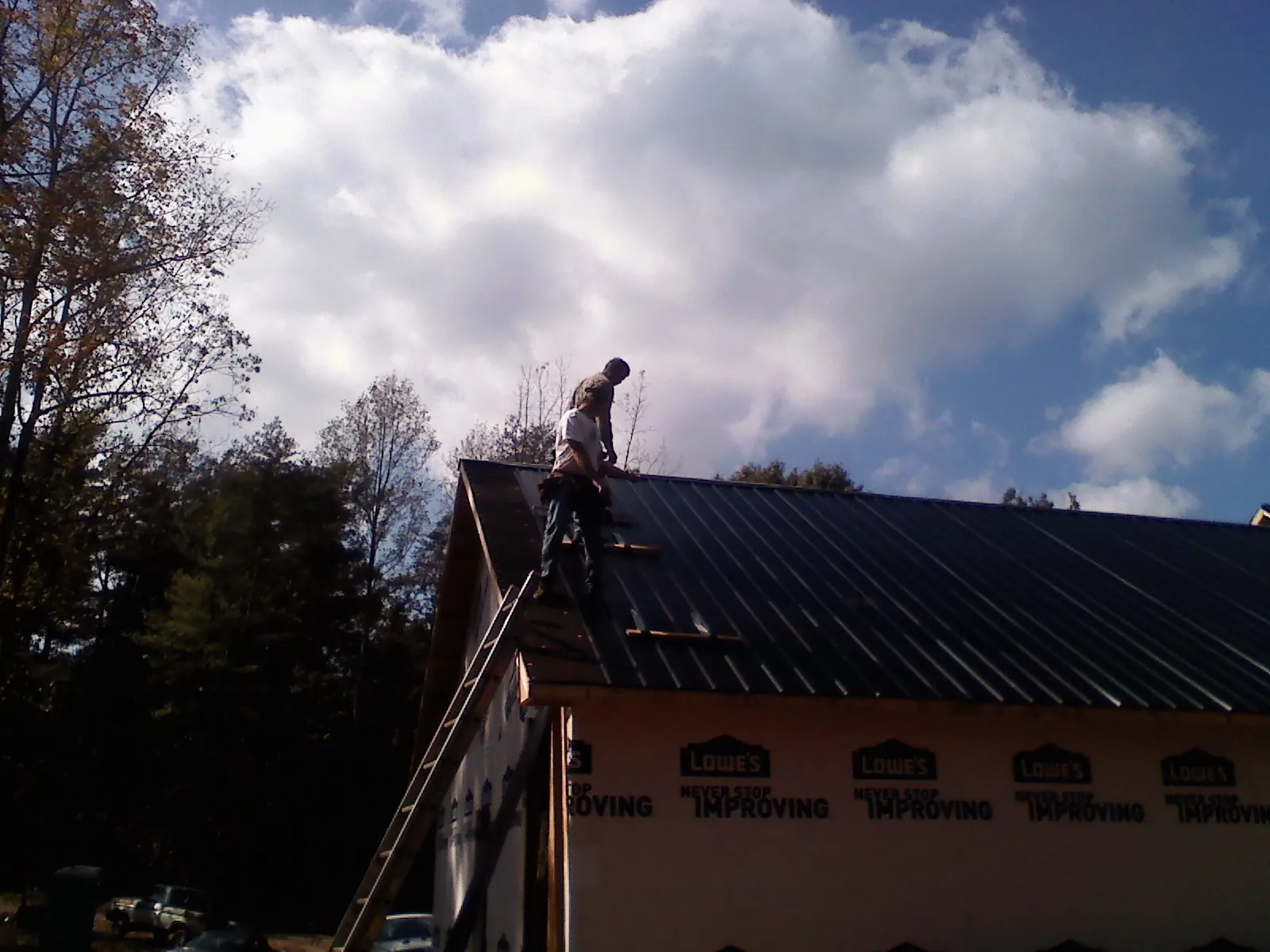 Roofer fastening dark metal panels high against a cloudy sky, from a Roof Inspection job in Waukomis