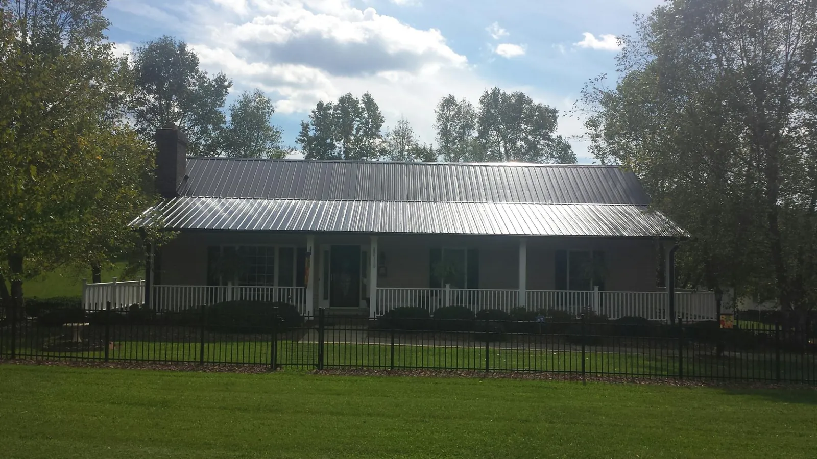 Gray metal roof on a brick ranch with a full width front porch — Gutter Guard Installation work by our crew in Waukomis