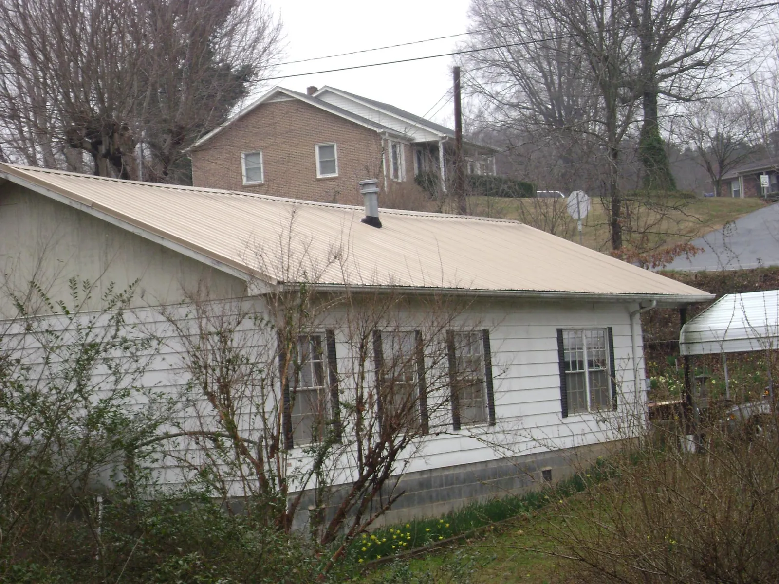 Tan metal roof on a white sided house set into a hillside — Commercial Roofing by Roofing Brothers in Waukomis